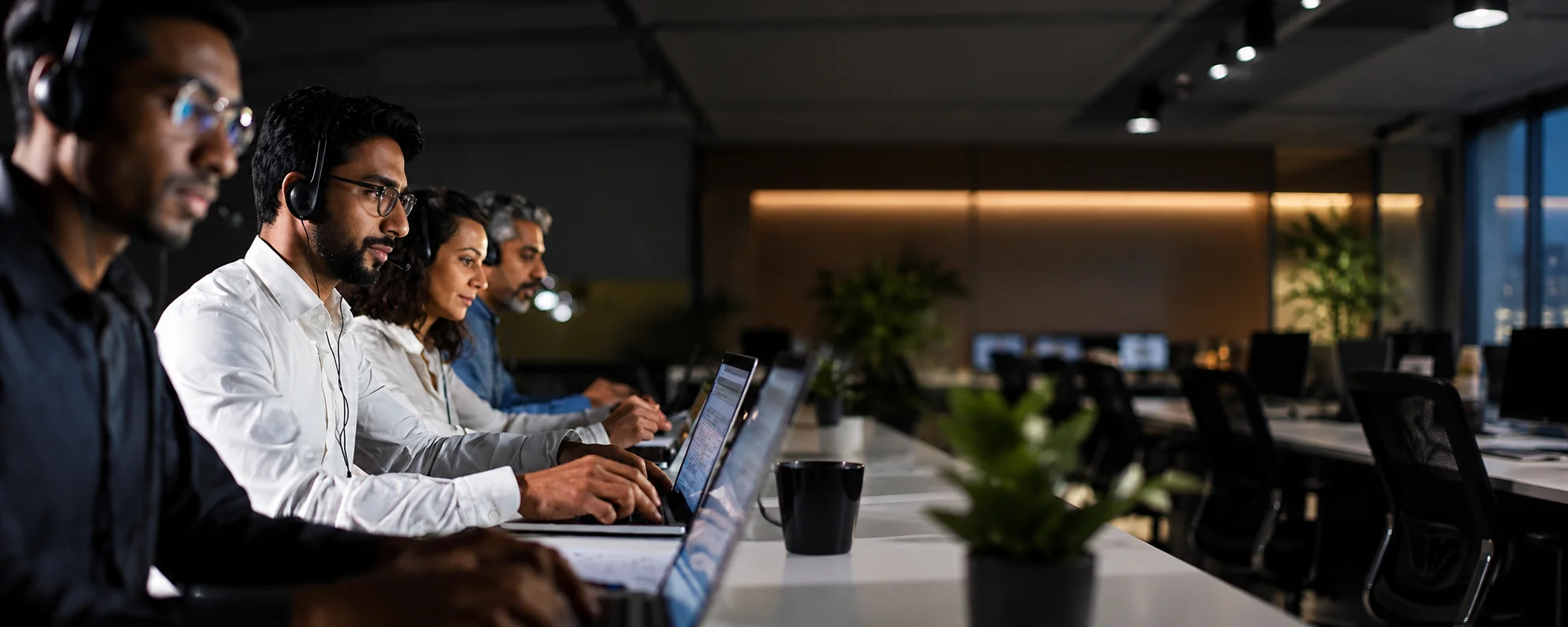 Corporate travel support team with headsets working on laptops in an office at night